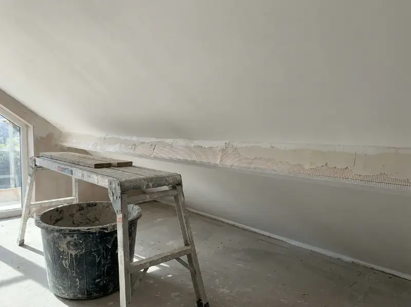 Pas geplakt wit plafond met een wapeningsnet dat nog zichtbaar is aan de rand, stelling en pleisterbak eronder