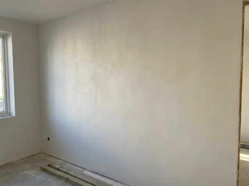 Binnenmuur met een fijne sierpleister in warm wit, strijklicht toont de structuur